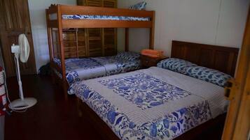 A room with two bunk beds, a wooden wardrobe, a bedside table with a lamp, and a fan.