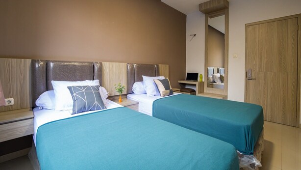 A hotel room with two beds, a desk, a laptop, and a mirror.
