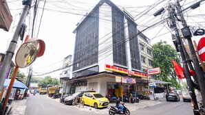 A building with a large glass facade, a visible Alimart store, and parked vehicles including a yellow car and motorcycles.