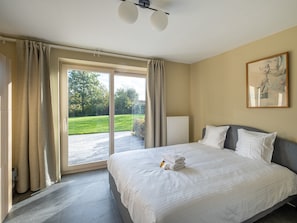 A hotel room with a bed, a radiator, a painting, and a view of a garden through a glass door. - Overijse Grande Residence (Overijse)