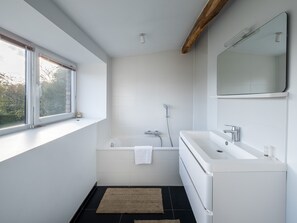 A modern bathroom with a bathtub, a large mirror, and a window. - Overijse Grande Residence (Overijse)