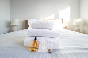 A neatly made bed with white linens, two white lamps, and a stack of white towels. - Overijse Grande Residence (Overijse)