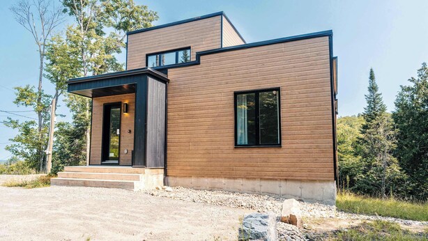 A modern two-story house with a wooden exterior, a front entrance with steps, and a visible window. - Yéti de Tremblant - Spa & Forest Charm (La Conception)