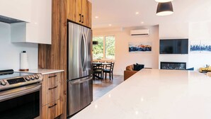 A modern kitchen with a stainless steel refrigerator, wooden cabinets, a built-in oven, and a dining area with a table and chairs. - Yéti de Tremblant - Spa & Forest Charm (La Conception)