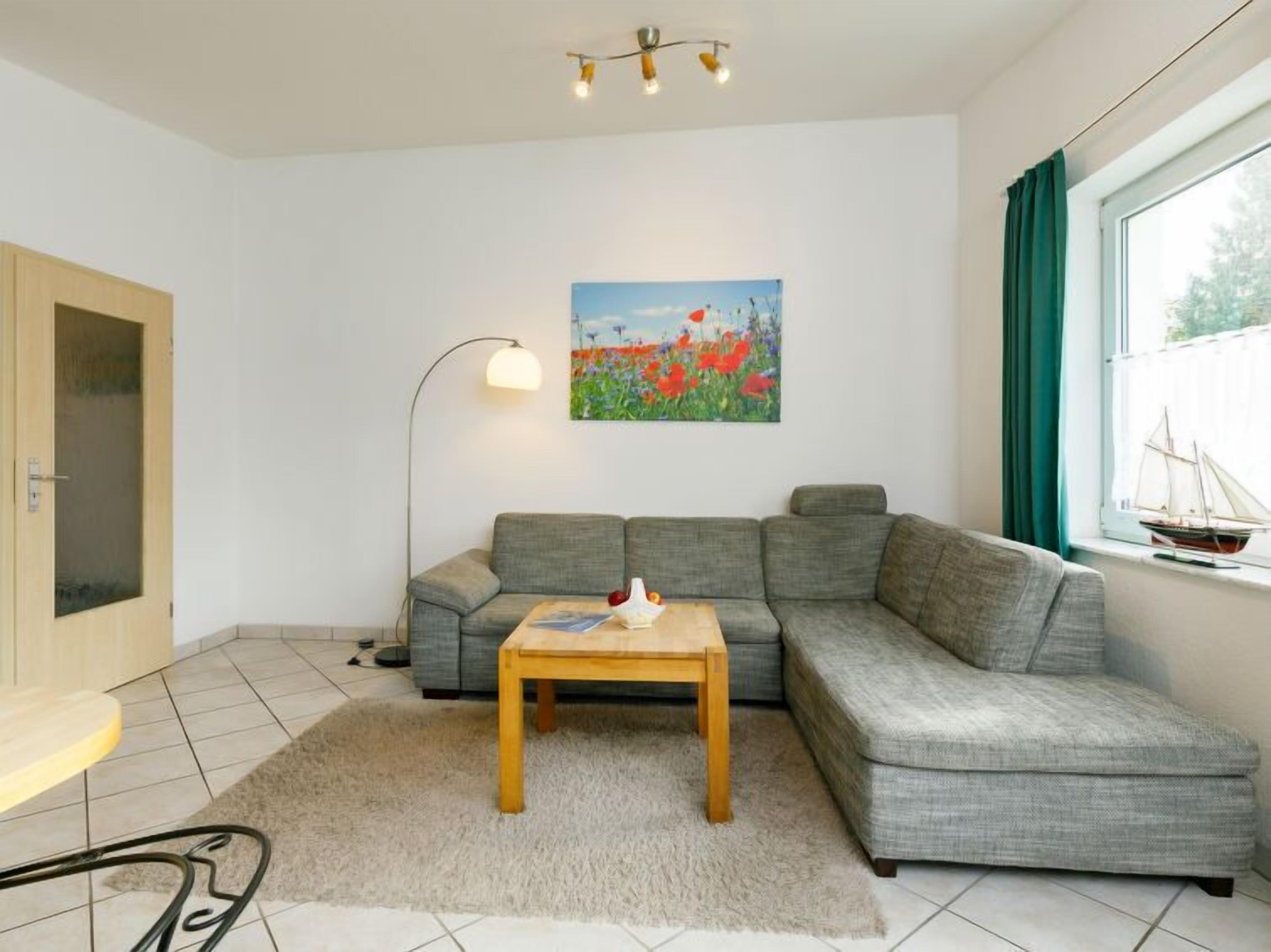A modern living room with a grey sectional sofa, a wooden coffee table, a floor lamp, and a painting of flowers on the wall.