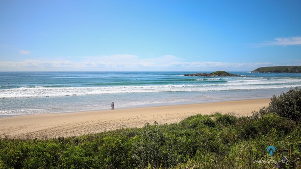 A beach with clear skies, calm waves, and a person walking along the shore.