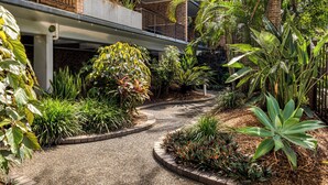 A courtyard with a gravel path, surrounded by various plants and a brick building with balconies.