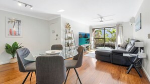 A modern living room with a glass dining table, grey chairs, a black sofa, and a ceiling fan.