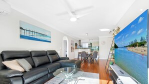 A living room with a black leather sofa, a glass coffee table, and a large flat-screen TV.