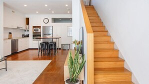 A modern kitchen with white cabinets, a wooden dining table, and a staircase with wooden steps.