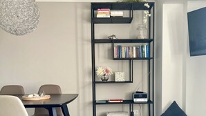 Ein stilvoller Essbereich mit einem dunklen Holztisch und Stühlen, einem Bücherregal mit Büchern und Dekoration sowie einem Korbkissen.
