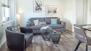 Ein modernes Wohnzimmer mit einem grauen Sofa, einem schwarzen Sessel und zwei runden schwarzen Beistelltischen.