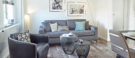 Una sala de estar moderna con un sofá gris, un sillón negro y dos mesitas redondas negras.