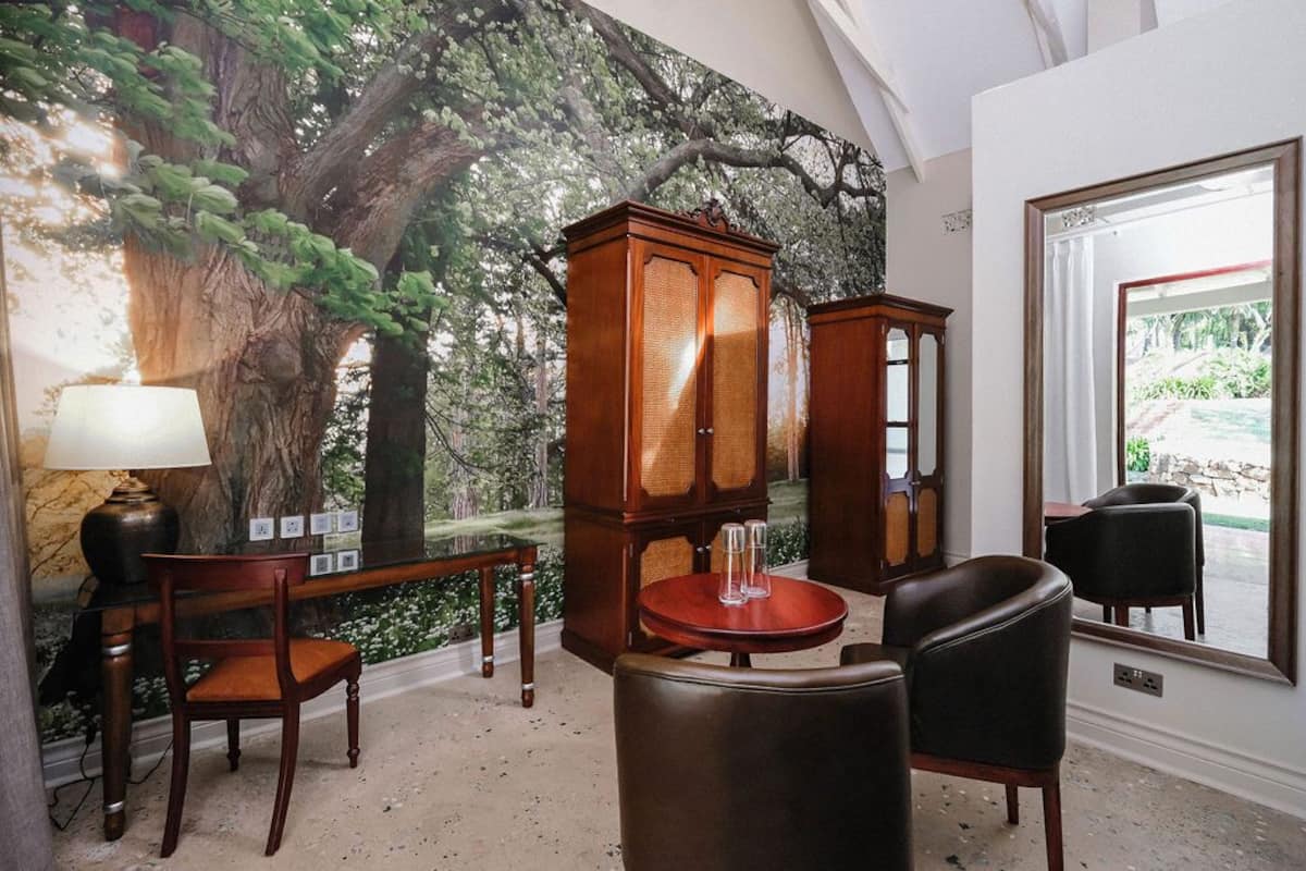 A room with a large mural of a tree, a wooden cabinet, a round table with chairs, and a lamp.