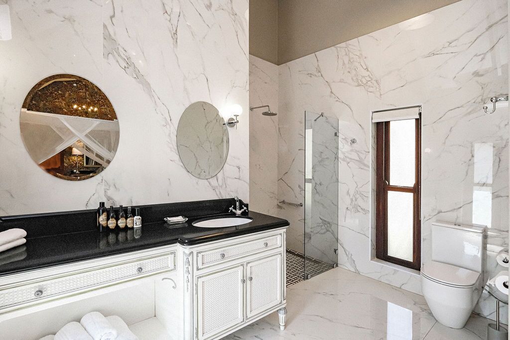 A modern bathroom with a marble vanity, a round mirror, a glass shower enclosure, and a toilet.