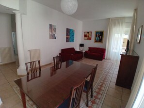 A dining area with a wooden table and chairs, a red sofa, and a lamp. - Corso Roma Apartament Gallipoli (Gallipoli)