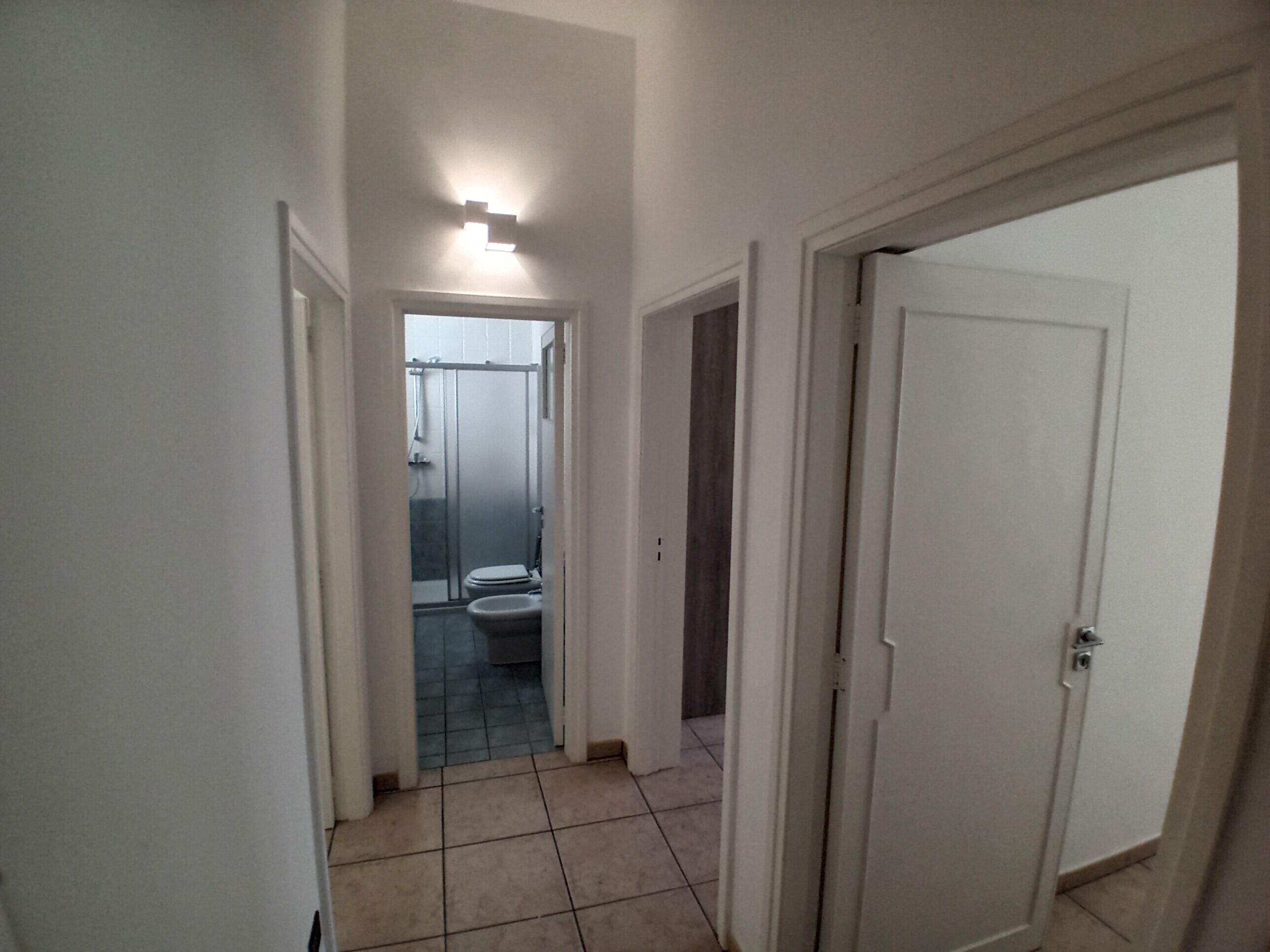 A narrow hallway with a bathroom visible in the distance, featuring a toilet and a shower area.