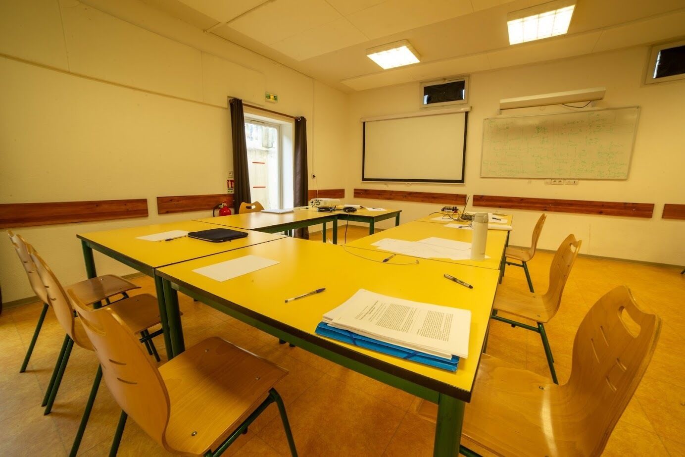 A conference room with a long table, chairs, a projector screen, and a whiteboard.