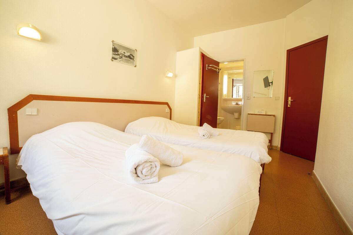 A hotel room with two beds, a bathroom, and a door.