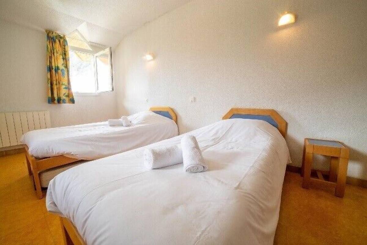 Two single beds with wooden headboards, white bedding, and a small wooden stool beside one bed.