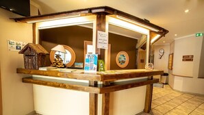 Un mostrador de recepción con estructura de madera, un espejo, una pequeña decoración de madera con forma de casa y folletos informativos.