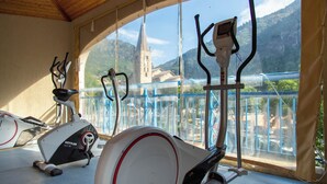 Gimnasio interior con bicicletas estáticas y vista a una iglesia a través de amplias ventanas.