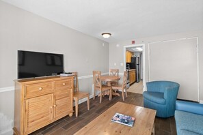 A living room with a TV, wooden furniture, a dining table, and a kitchen in the background. - Roomy Oceanfront Suite: Includes Breakfast 7th Flr (Myrtle Beach)