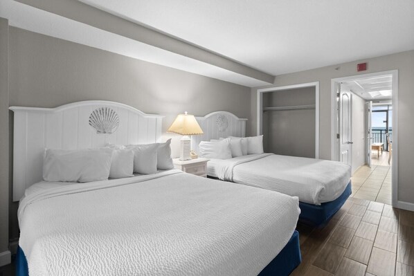 A hotel room with two beds, a nightstand with a lamp, and a view of the sea through an open door. - Roomy Oceanfront Suite: Includes Breakfast 7th Flr (Myrtle Beach)