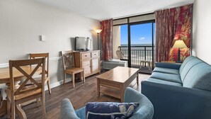 A living room with a sofa, chairs, a coffee table, a TV, and a balcony with curtains. - Spacious Oceanfront Ste with Breakfast 7th Flr (Myrtle Beach)