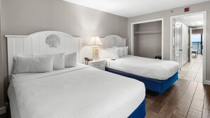 Une chambre d’hôtel avec deux lits, une table de chevet, une lampe et une vue sur la mer, visible par une porte ouverte.