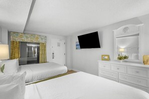 A hotel room with a bed, a TV mounted on the wall, a dresser, and a window with curtains. - Astonishing Oceanfront Suite: 7th Flr W Breakfast (Myrtle Beach)
