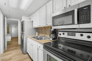 A compact kitchen with white cabinets, a microwave, a stove, and a coffee maker. - Astonishing Oceanfront Suite: 7th Flr W Breakfast (Myrtle Beach)