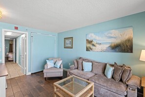 A living room with a couch, chair, and a glass coffee table. There is a painting on the wall and a door leading to another room. - Magnificent Oceanfront Ste: Includes Breakfast (Myrtle Beach)