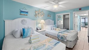 A room with two beds, a ceiling fan, and a view of the ocean.