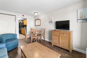 A living room with a blue sofa, wooden dining table, and TV on a wooden cabinet. - Mesmerizing Oceanfront Suite w/Breakfast 7th Flr (Myrtle Beach)