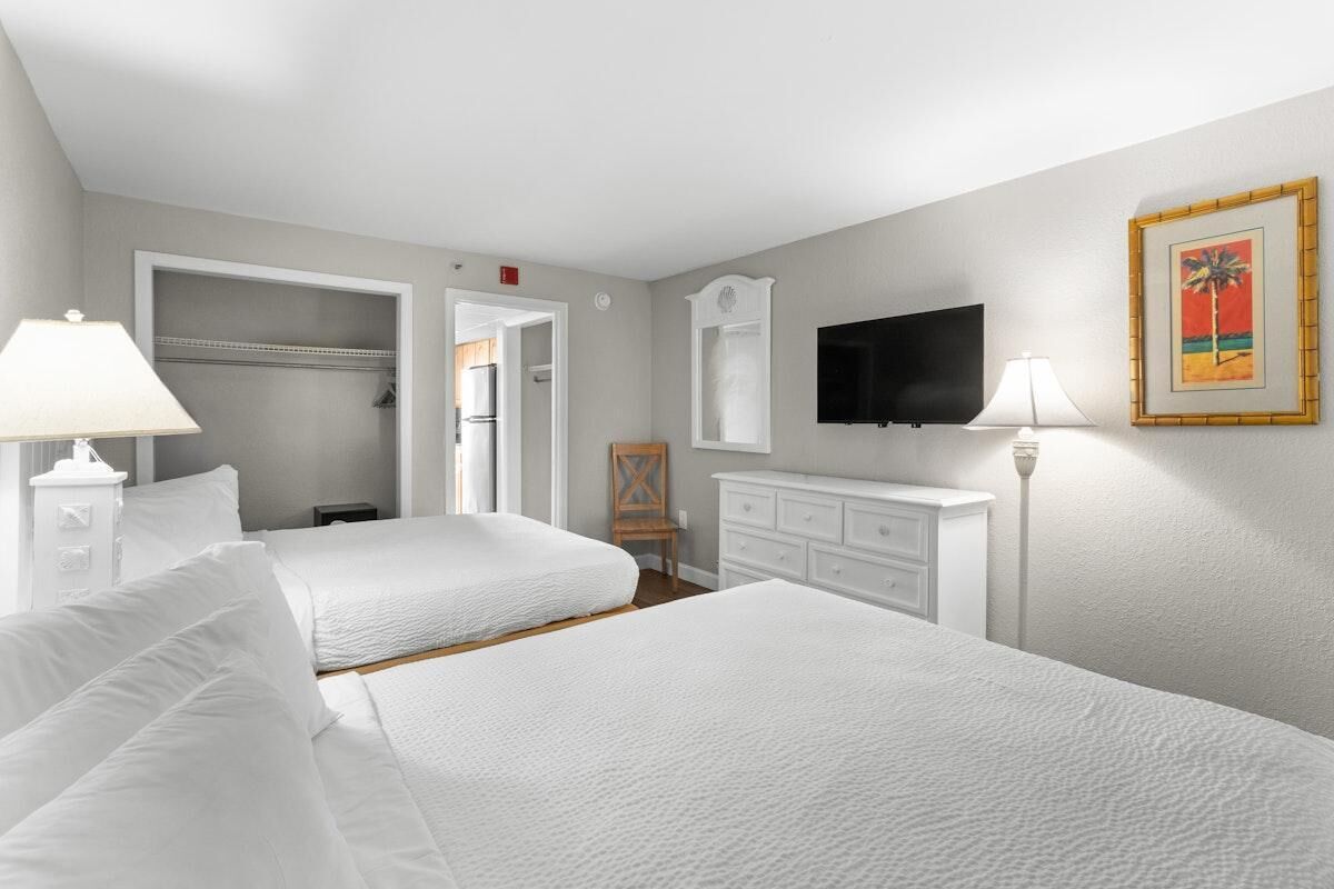 A hotel room with two beds, a TV, a wardrobe, and a painting on the wall.