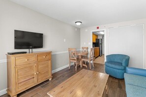 A living room with a wooden cabinet, a television, a dining table with chairs, and a blue armchair. - Majestic Oceanfront Ste: Includes Breakfast (Myrtle Beach)