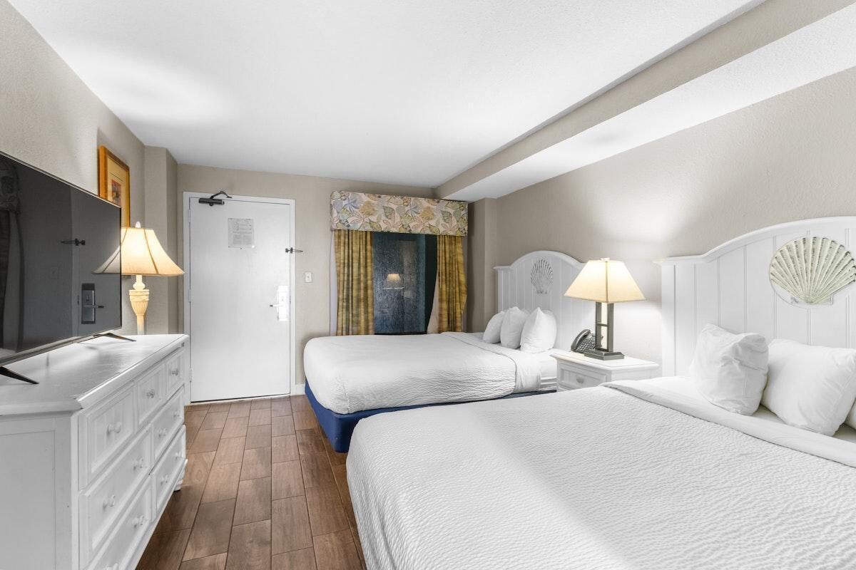 A hotel room with two beds, a TV, a dresser, and a door with a note.