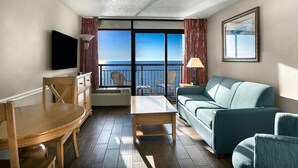 A hotel room with a balcony, a sofa, a dining table, and a TV. - Awe Inspiring Oceanfront Suite w/Breakfast 8th Flr (Myrtle Beach)