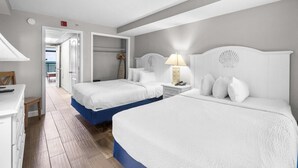 A hotel room with two beds, a desk, and a chair. There is a hallway leading to another room. - Beachy Oceanfront Suite with Breakfast 8th Floor (Myrtle Beach)