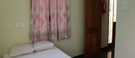 Una habitación con cama, una puerta y una pared con toma de corriente.