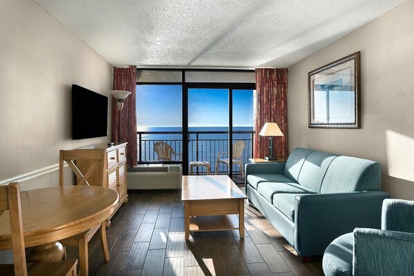 A hotel room with a balcony, a sofa, a dining table, and a TV. - Astonishing Oceanfront Ste, 9th Flr, Breakfast (Myrtle Beach)