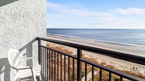 A balcony with a white chair, overlooking a beach with sand and water. - Mesmerizing Oceanfront Ste 9th Flr Free Breakfast (Myrtle Beach)