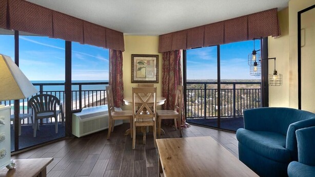 Une pièce avec un plancher en bois, un canapé bleu, une table en bois et une chaise. Il y a une fenêtre donnant sur l’océan.