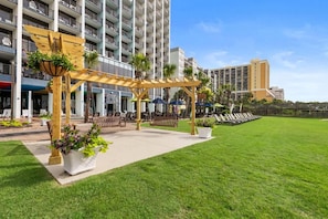 A hotel courtyard with a pergola, seating areas, and a grassy lawn. - Exquisite Ocean View Suite Free Breakfast 12th Flr (Myrtle Beach)