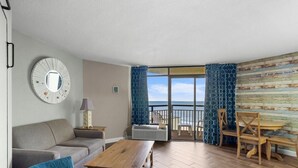 Ein Wohnzimmer mit Sofa, Couchtisch und Meerblick durch eine Glastür.