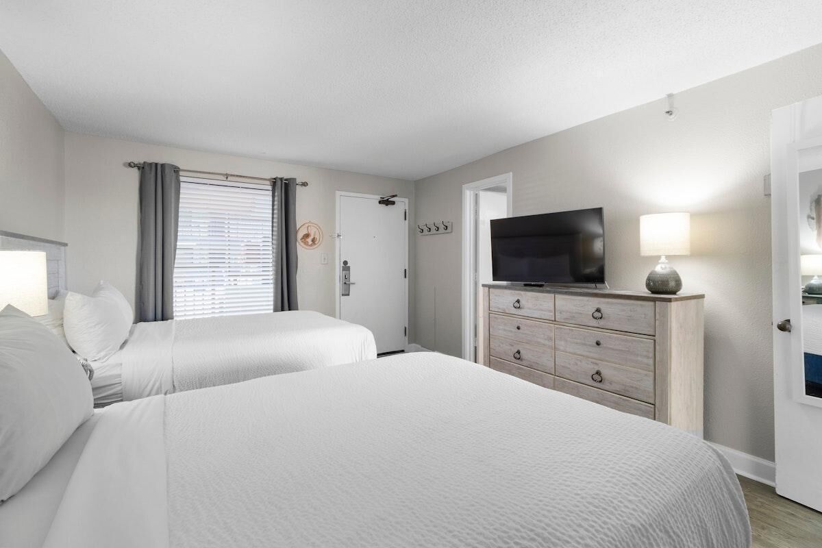 A hotel room with two beds, a TV, a dresser, and a door.