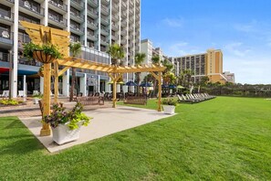 A hotel courtyard with a pergola, seating areas, and a grassy lawn. - Elevated Serenity: Ocean View Ste Free Breakfast (Myrtle Beach)