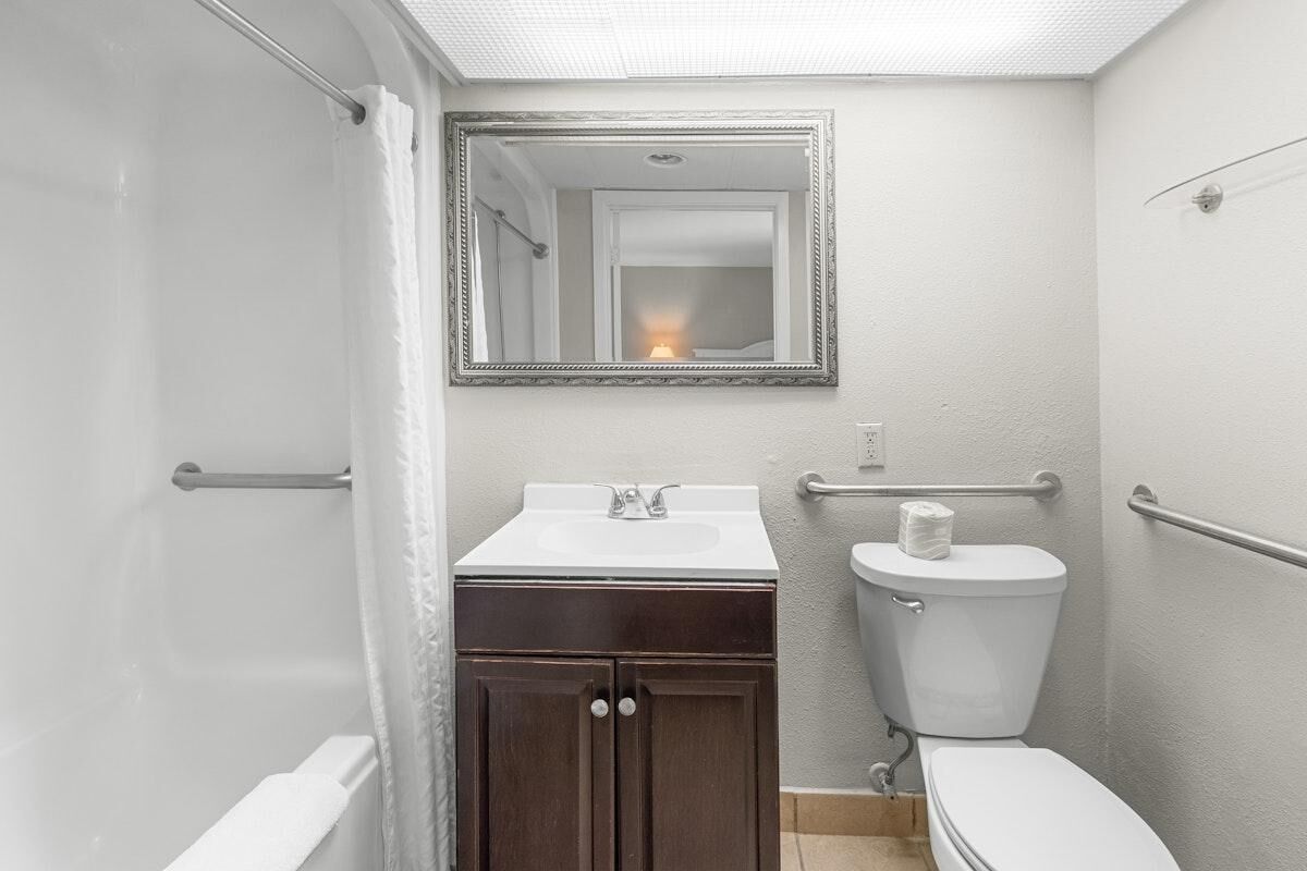 A bathroom with a white sink, dark wooden cabinet, white toilet, and a mirror above the sink.