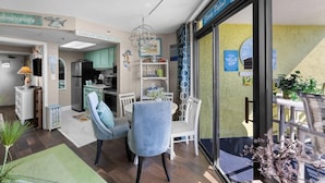 A modern kitchen with a refrigerator, stove, and dining area with chairs and a table. - Jaw-Dropping Ocean View King Ste w/Breakfast (Myrtle Beach)